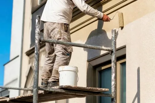 Painter on scaffolding painting a light exterior wall